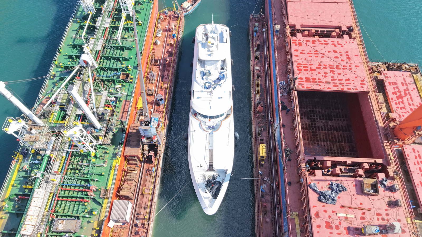 A superyacht alongside in the Tuzla shipyard district for refit, seen from above, with commercial hulls at the neighbouring quays