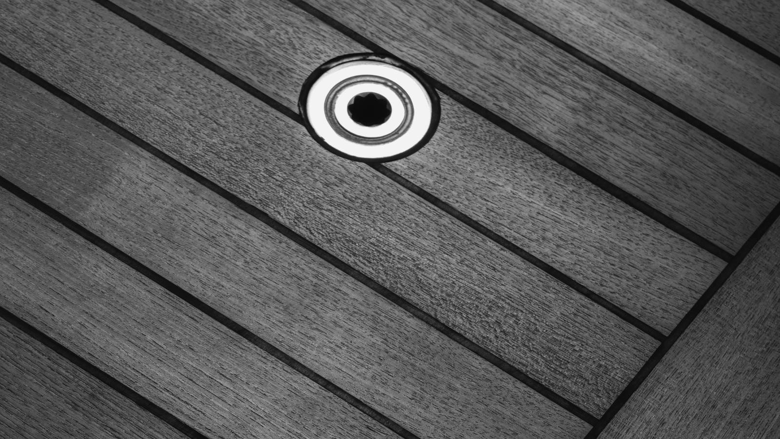 Close view of a teak deck, caulked seams running into a curved margin board with a flush stainless deck socket set through the planking
